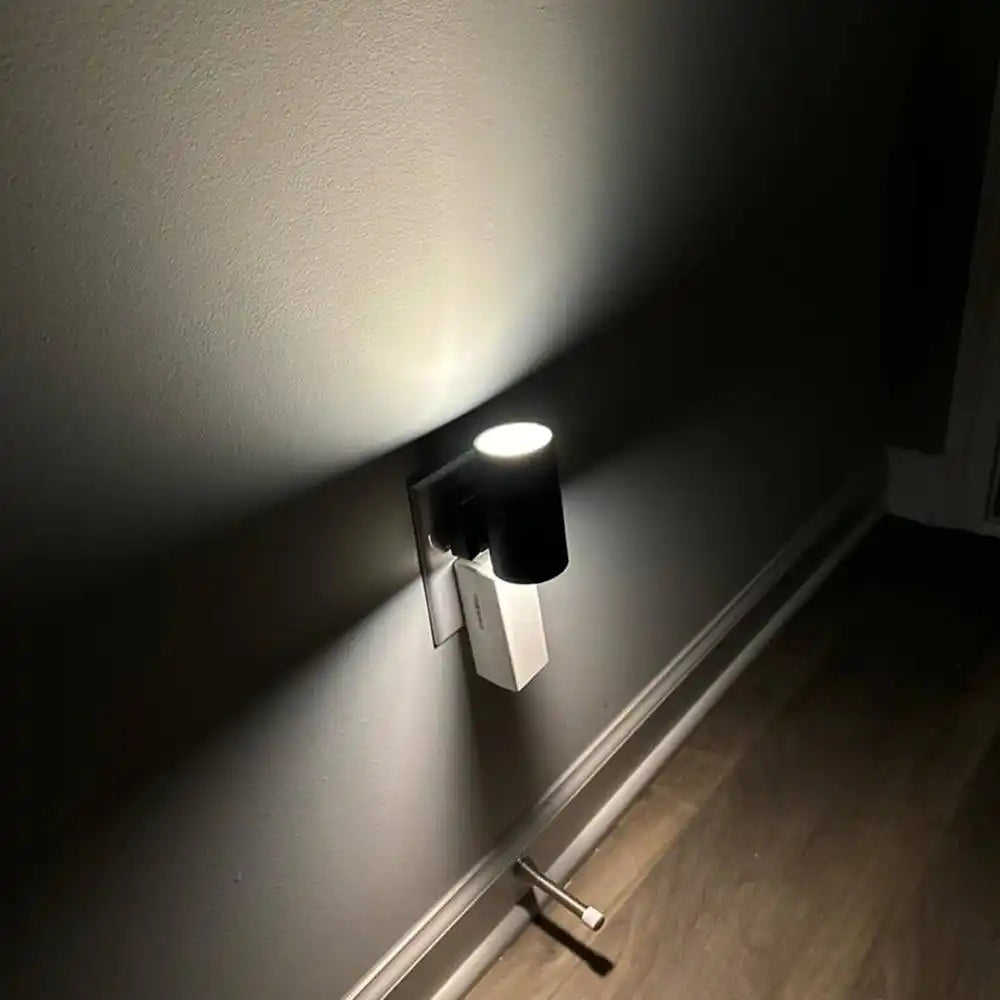 A black and white plug-in night light with an upward-facing lamp.