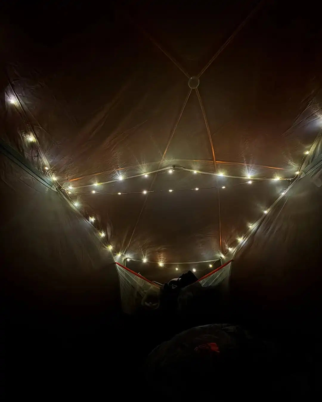 A dark tent interior illuminated by a triangular string of warm fairy lights.