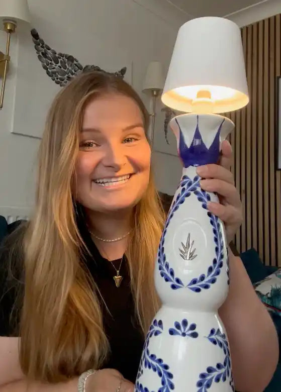 A decorative bottle lamp with a white lampshade and blue floral patterns.