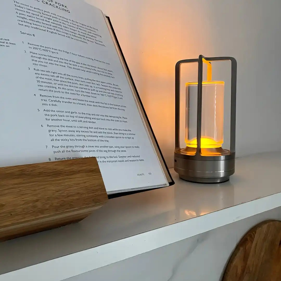 A modern, portable lantern with a warm, glowing light source, enclosed in a clear cylinder and a dark metal frame.