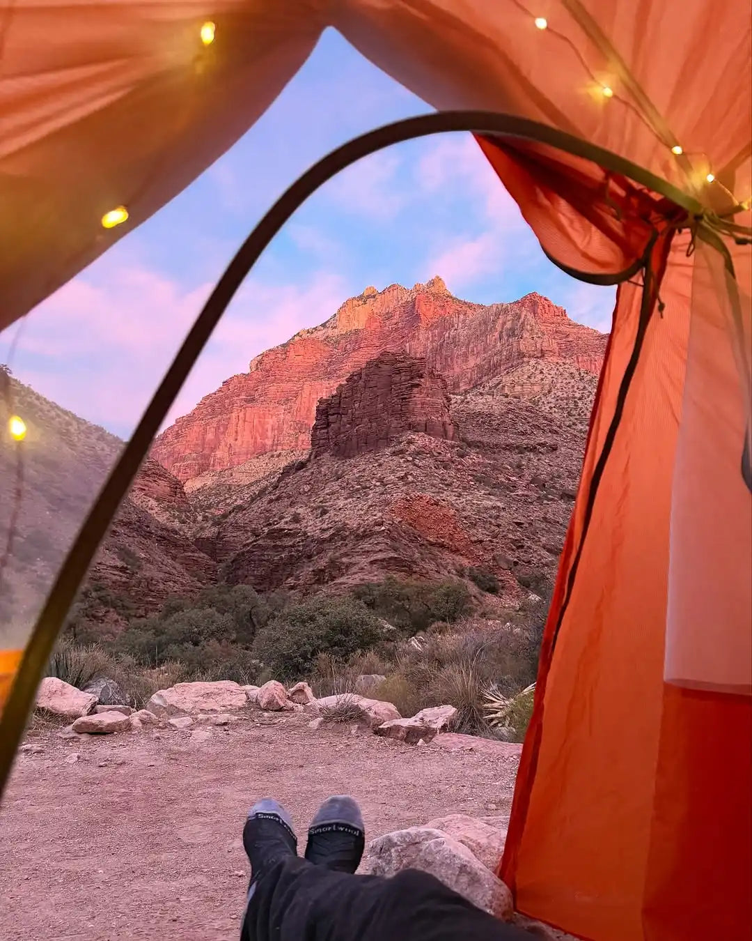 An orange tent with string lights, viewed from the inside looking out at a mountainous landscape.