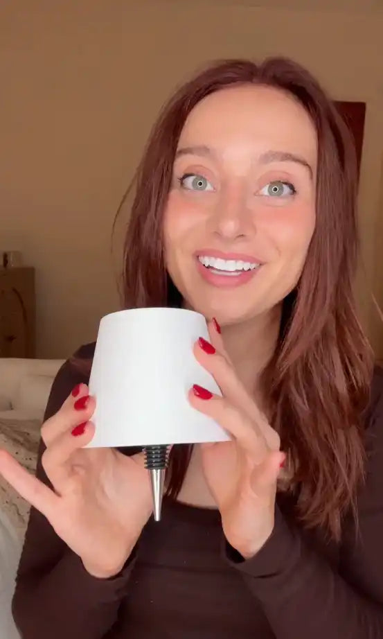 A woman holding a white, conical bottle pourer with a metallic spout.